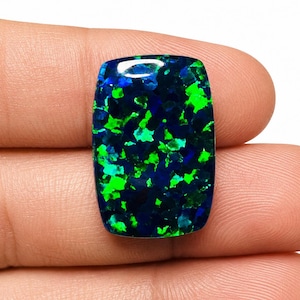 May include: A rectangular black opal gemstone featuring a polished surface with vibrant, scattered flashes of neon green and deep blue color play throughout the stone, showcasing a high-gloss finish and a distinct, multi-faceted internal pattern.