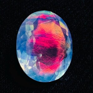 May include: An oval-shaped faceted gemstone with a translucent, milky white base and a prominent, vibrant red and orange play-of-color flash concentrated in the center. The stone features a geometric, multi-faceted surface that reflects light.