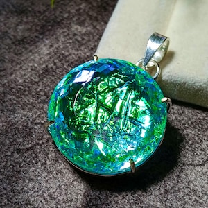May include: A round pendant featuring a faceted, iridescent stone with vibrant green and blue hues. The stone has a cracked, reflective texture and is secured in a silver-toned metal setting with four prongs and a top bail for attachment to a chain.