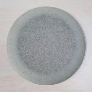 Może przedstawiać: Okrągły, szary talerz o teksturowanej powierzchni. Talerz ma lekko podniesiony brzeg i matowe wykończenie. Talerz wykonany jest z materiału kompozytowego i nadaje się do serwowania potraw.