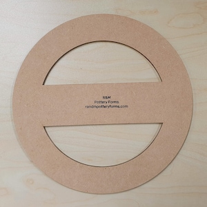May include: A circular pottery form made of light brown wood. The form has a large circular opening with a horizontal bar across the centre. The text "R&M Pottery Forms randmpotteryforms.com" is printed on the form.