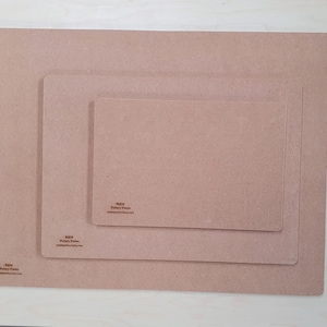 May include: Three light brown rectangular placemats of different sizes are nested together. The placemats have rounded corners and a smooth surface. The smallest placemat has the text "R&M Pottery Forms" printed on it.