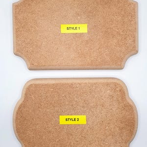 May include: Two unfinished wooden plaques with decorative edges. The top plaque is rectangular, and the bottom plaque has a more rounded shape. Each plaque has a yellow sticker with the text "STYLE 1" and "STYLE 2" respectively.