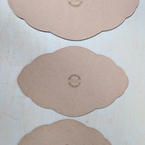 Może przedstawiać: Trzy drewniane tace do serwowania w kształcie chmury w różnych rozmiarach. Tace są w kolorze jasnobrązowym z ciemnobrązową krawędzią. Każda taca ma okrągłe logo z napisem "RM POTTERY FORMS" wydrukowanym na spodzie.