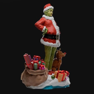 Puede incluir: Figura de un personaje verde con un traje de Papá Noel rojo con ribete de piel sintética blanca, cinturón negro y gorro rojo. Un saco marrón de regalos y un perro marrón con nariz roja están a los pies del personaje.