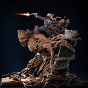 Op de afbeelding: Een gedetailleerd beeld van Rocket Raccoon die een wapen afvuurt, bovenop een Groot-figuur. Rocket draagt een blauw en rood uniform. De Groot-figuur is bruin en boomachtig, met een steenachtige structuur erachter. De basis is een boek.