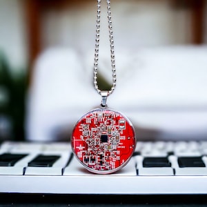 Può includere: Una collana con catena d'argento con un ciondolo circolare rosso che presenta un design di circuito stampato.