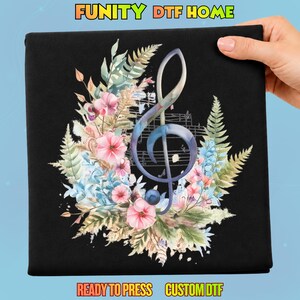 May include: A black fabric sheet featuring a central watercolor-style treble clef graphic overlaid on musical staff lines, surrounded by a vibrant arrangement of pink flowers, blue blossoms, and green fern leaves with the text FUNITY DTF HOME.
