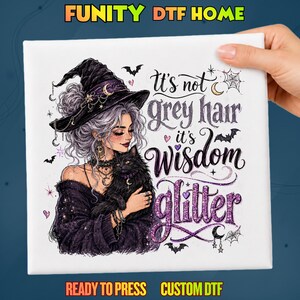 May include: A white DTF transfer sheet featuring a graphic of a person with grey hair wearing a witch hat and holding a black cat. The text reads: It's not grey hair it's Wisdom glitter. The design includes purple and black accents, bats, stars, and spiderwebs.