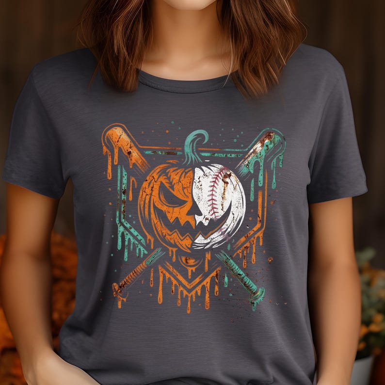 May include: A charcoal gray t-shirt featuring a graphic print of a split pumpkin and baseball design. The pumpkin is orange on one side and white like a baseball on the other, with two crossed baseball bats behind it in orange and teal.