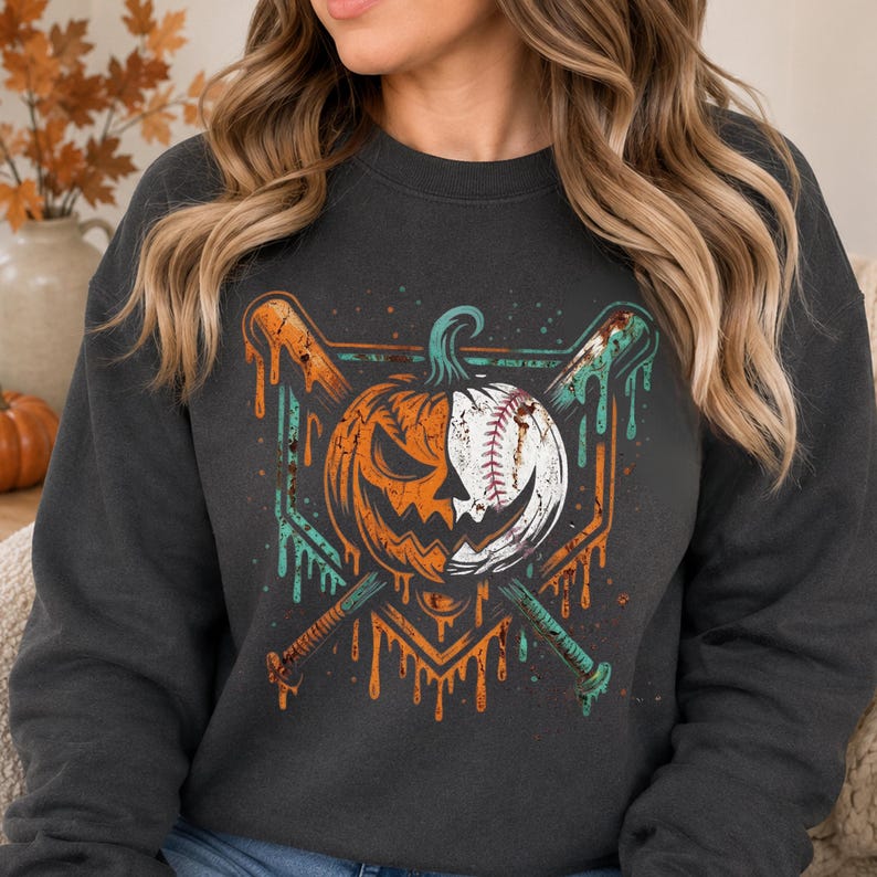 May include: A charcoal gray crewneck sweatshirt featuring a graphic print of a pumpkin split with a baseball design. The pumpkin is positioned in front of two crossed baseball bats, with orange and teal paint drip effects surrounding the design.