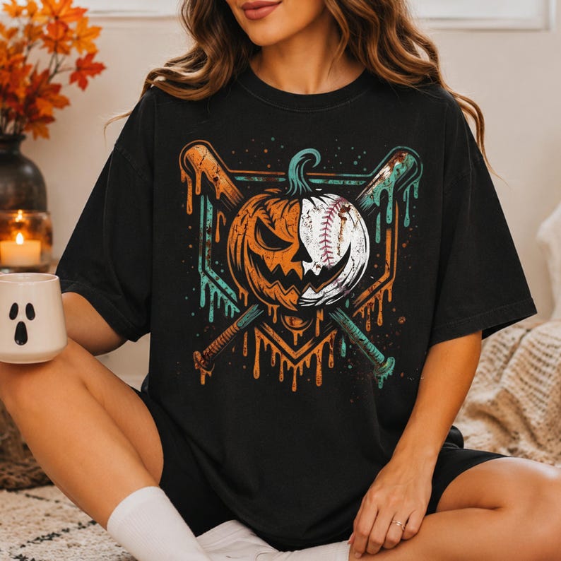 May include: A black t-shirt featuring a graphic print of a pumpkin and baseball hybrid design split down the middle, positioned over two crossed baseball bats. The artwork includes dripping paint effects in orange and teal colors on a dark background.