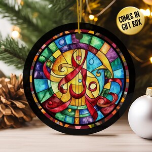 May include: A round Christmas ornament with a stained glass design. The ornament features a colorful abstract design with red, yellow, blue, and green hues. The ornament has a black border and a gold string for hanging. The text "COMES IN GIFT BOX" is on the upper right.