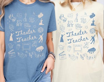 May include: Two t-shirts, one blue and one cream, featuring a theater-themed design. The design includes icons of stage lights, a film reel, a piano, and the text "Theater Teacher". The blue shirt has a slightly darker hue than the cream shirt.