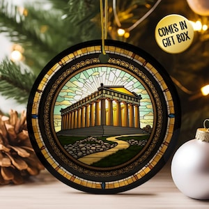 May include: Round Christmas ornament with a stained-glass design featuring a classical building with columns. The ornament has a black border with gold accents and a gold hanging string. The text "COMES IN GIFT BOX" is in a yellow circle.