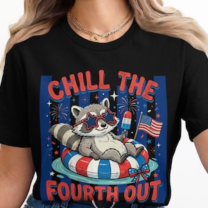 May include: Black t-shirt featuring a cartoon raccoon wearing star-shaped sunglasses, relaxing on a red, white, and blue inflatable ring. The shirt has the text "CHILL THE FOURTH OUT" and an American flag.
