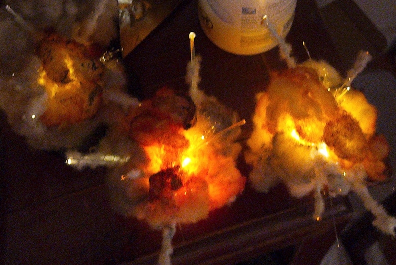 Pu&ograve; includere: Tre ornamenti decorativi luminosi composti da grappoli di materiale bianco simile al cotone, illuminati dall'interno da luci LED color arancione e giallo caldo, con sottili punte trasparenti che sporgono dal centro di ogni pezzo.