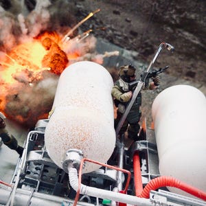 Pu&ograve; includere: Un diorama con due action figure di soldati in miniatura con equipaggiamento tattico posizionate vicino a due grandi serbatoi cilindrici bianchi. Un soldato impugna un fucile mentre sullo sfondo si vede un effetto di esplosione arancione.