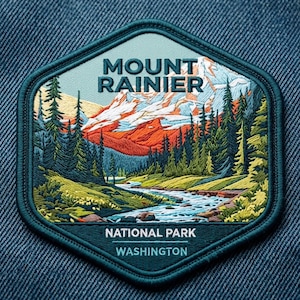 May include: A hexagonal embroidered patch featuring a landscape of Mount Rainier with snow-capped peaks, a flowing river, and evergreen trees. The text reads MOUNT RAINIER NATIONAL PARK WASHINGTON in white lettering against a dark teal border.