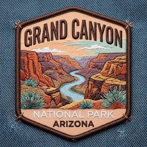 May include: A hexagonal embroidered patch featuring a landscape of the Grand Canyon with a winding blue river, red rock formations, and green desert plants. The text reads GRAND CANYON NATIONAL PARK ARIZONA in dark brown and white lettering.