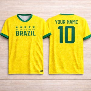 Peut inclure: Un maillot de football jaune du Br&eacute;sil avec des bordures vertes. Il affiche "BRAZIL" et les ann&eacute;es 1968, 1992, 1970, 1994 et 2002. Le dos porte "YOUR NAME" au-dessus du num&eacute;ro 10 en vert.