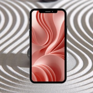 May include: A black smartphone displays a pink abstract design on its screen. The phone rests on a small, gray stone, set against a backdrop of a sand garden with curved lines.