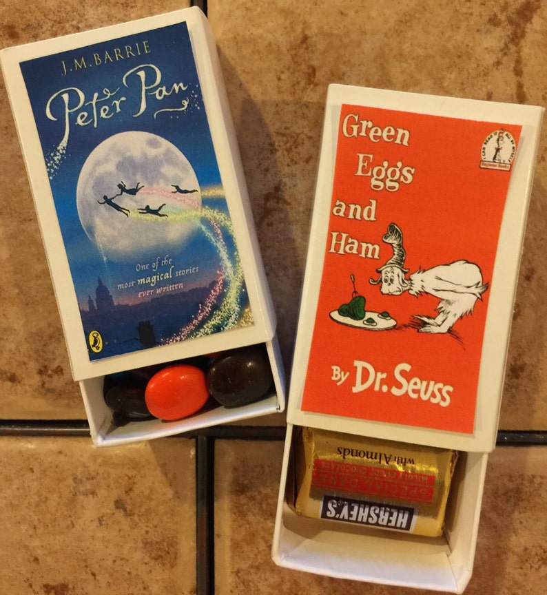 May include: Two matchbox-style boxes with book covers. The first box has a blue cover with a moon and stars, and the text "J.M. Barrie Peter Pan". The second box has a red cover with the text "Green Eggs and Ham by Dr. Seuss". Both boxes have candy inside.