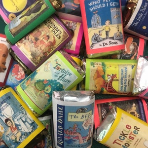 K&ouml;nnte beinhalten: Eine Sammlung verpackter Schokoladentafeln mit verschiedenen Kinderbuchcovern. Die Cover zeigen Illustrationen von Tieren, Menschen und Szenen aus den Geschichten. Einige der Titel sind "Die Schildkr&ouml;te und der Hase", "Der BFG", "Welches Haustier soll ich mir holen?", "Grimms M&auml;rchen" und "Der kleine Prinz".