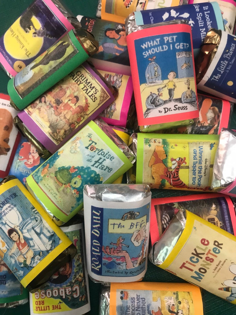 K&ouml;nnte beinhalten: Eine Sammlung verpackter Schokoladentafeln mit verschiedenen Kinderbuchcovern. Die Cover zeigen Illustrationen von Tieren, Menschen und Szenen aus den Geschichten. Einige der Titel sind "Die Schildkr&ouml;te und der Hase", "Der BFG", "Welches Haustier soll ich mir holen?", "Grimms M&auml;rchen" und "Der kleine Prinz".