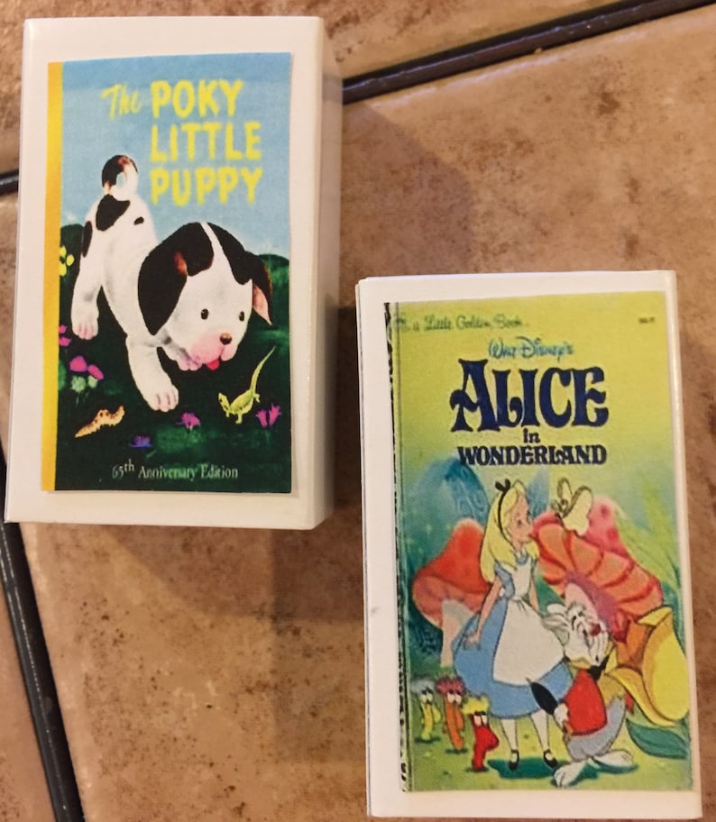 May include: Two miniature book covers. The first cover is blue and yellow with a black and white puppy on it. The title is "The Poky Little Puppy" and the text "65th Anniversary Edition" is at the bottom. The second cover is yellow and green with a picture of Alice from Alice in Wonderland. The title is "Walt Disney's Alice in Wonderland".