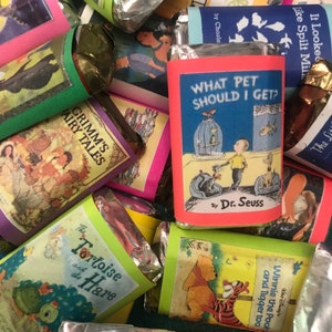 K&ouml;nnte beinhalten: Eine Sammlung von verpackten Schokoladenriegeln mit bunten Buchumschl&auml;gen, die beliebte Kindergeschichten zeigen, darunter "Welches Haustier soll ich mir holen?" von Dr. Seuss, "Die Schildkr&ouml;te und der Hase", "Winnie Puuh und Tigger auch" und "Grimms M&auml;rchen".