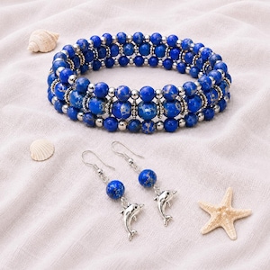 May include: A multi-strand bracelet composed of round blue marbled beads and small silver-toned spacer beads, accompanied by a pair of matching drop earrings featuring a single blue marbled bead and a silver-toned dolphin charm on a hook wire.