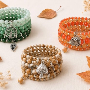 May include: Three multi-strand beaded bracelets. One features green beads with a silver tree charm and leaf charm. Another has orange beads with a silver pumpkin charm. The third consists of tan speckled beads with a silver mushroom charm.