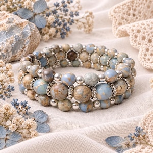 May include: A multi-strand bracelet composed of round, variegated blue and tan stone beads interspersed with small, polished silver-toned metal spacer beads. The beads feature natural marbling patterns in shades of sky blue, beige, and brown.