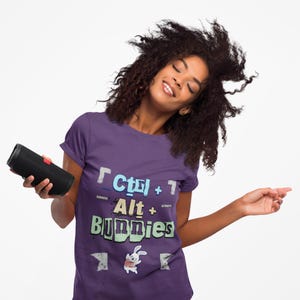 May include: Purple t-shirt with the text "Ctrl + Alt + Bunnies" in a pixelated font. The shirt features a graphic of a cartoon bunny. A black portable speaker with a red accent is held in the left hand.