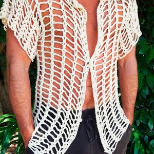 May include: An off-white, short-sleeved, button-down shirt featuring an open-work crochet construction with a grid-like pattern and a classic collar. The garment is worn over the torso and includes the text PDF UknitMe2 in the bottom corner.