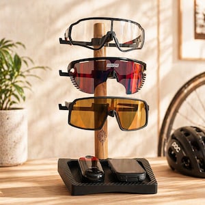 May include: A wooden sunglasses display stand holding three pairs of sunglasses. The top pair has clear lenses, the middle pair has red lenses, and the bottom pair has orange lenses. A small black tray at the base holds a black device and a red and black device.