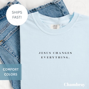 May include: A light blue t-shirt with the text "JESUS CHANGES EVERYTHING." The shirt is made of Comfort Colors material and is displayed on top of blue denim jeans.