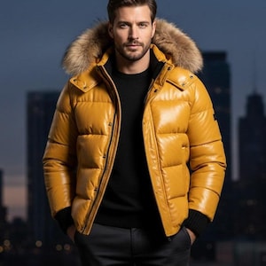 Könnte beinhalten: Senfgelbe Steppjacke mit fellbesetzter Kapuze. Die Jacke hat ein glänzendes, gestepptes Aussehen und einen schwarzen Reißverschluss. Die Person im Bild trägt einen schwarzen Pullover und eine dunkle Hose. Der Hintergrund zeigt eine verschwommene Stadtlandschaft.