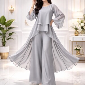 Könnte beinhalten: Hellgraues zweiteiliges Outfit mit einem Oberteil mit ausgestellten Ärmeln und einer Hose mit weitem Bein. Das Oberteil hat ein fließendes, mehrschichtiges Design, die Hose ist bodenlang. Das Outfit ist aus leichtem Stoff gefertigt, ideal für formelle Anlässe.