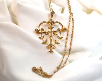 Könnte beinhalten: Eine goldfarbene Halskette mit Anhänger, die ein herzförmiges Design mit floralen und blattartigen Akzenten aufweist. Der Anhänger ist mit kleinen, runden, perlenartigen Verzierungen versehen. Die Halskette hat ebenfalls eine goldfarbene, zarte Kette.