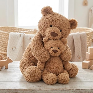 Può includere: Due orsacchiotti marroni, uno grande e uno piccolo, sono seduti insieme. L'orso più grande abbraccia quello più piccolo. Entrambi hanno nasi marroni e occhi scuri. Gli orsi sono fatti di un materiale morbido e peluche.