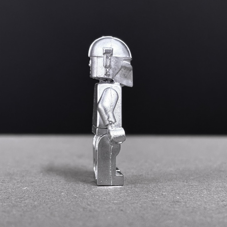 May include: A silver-colored minifigure with a helmet and armor. The figure is standing upright, with arms at its sides. The helmet has a distinctive shape, and the figure appears to be made of metal.