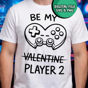 May include: White t-shirt with a black graphic of a heart-shaped game controller. The text reads "BE MY VALENTINE PLAYER 2" in black, with "VALENTINE" crossed out. A digital file SVG & PNG is in the top right corner.