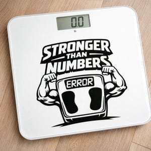 May include: A white digital bathroom scale with the text "STRONGER THAN NUMBERS" and a graphic of muscular arms. The scale displays "0.0 lb". The design includes the word "ERROR" on the scale's display, and two black foot pads.