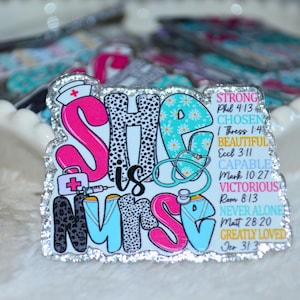 May include: A decorative badge with the words "She is Nurse" in pink, black, and turquoise, with a nurse's hat, medical equipment, and inspirational words. The badge has a silver glitter border and is on a white surface.