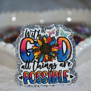 May include: A glitter-edged badge with the words "With God all things are possible." The design features a colorful sunflower and butterflies. The letters "G" and "D" are in a rainbow gradient. The background is a white, scalloped dish.