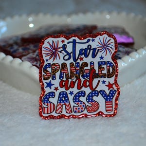 以下が含まれることがあります： 赤、白、青で「Star Spangled and Sassy」の文字が入った愛国的なテーマの装飾ステッカー。 ステッカーはキラキラ光る赤い縁取りで、星と花火が特徴です。 白いハート型の皿に入っています。