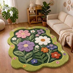May include: A floral-shaped rug with a green border and a dark green interior. The rug features large, colourful flowers in pink, white, purple, orange, and blue, with green leaves. The rug is placed on a wooden floor.