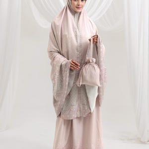 May include: A light pink prayer outfit, comprising a head covering, long-sleeved top, and skirt, with a matching drawstring bag. The outfit has a subtle patterned design and is made of a soft, flowing fabric.